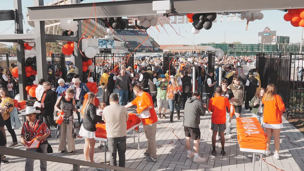 A group of people gather in front of a sports stadium and mingle.