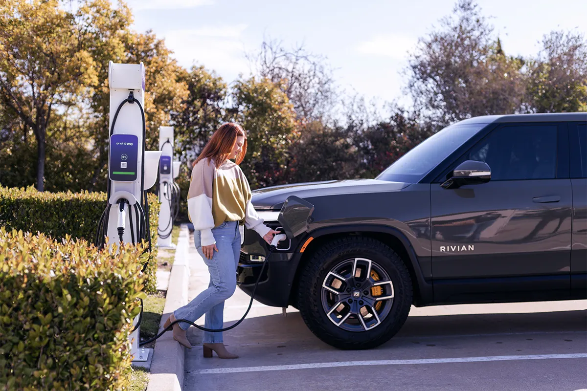 Several vehicles lined up along a curb are blurred while in the foreground a white and silver electric vehicle charger is in focus.