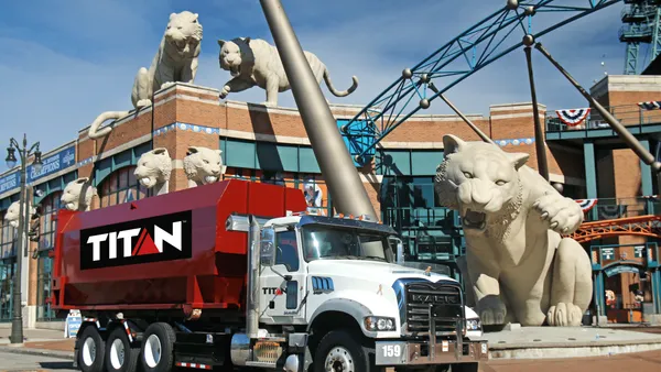 A red waste truck with the Titan Environmental logo in front of a stadium with tiger statues
