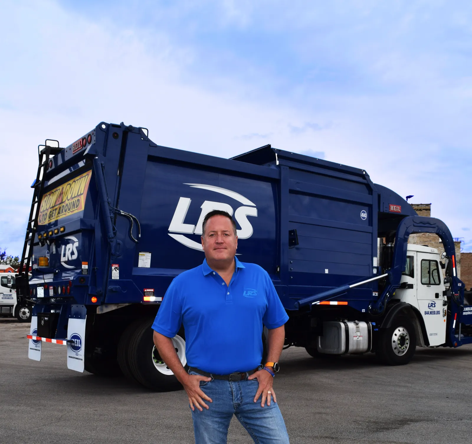 Man in blue polo standing in front of blue garbage truck