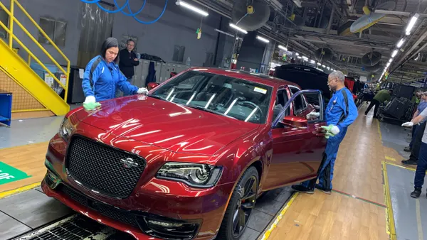 Auto workers inspect and wipe a red car rolling off a production line at a factory.
