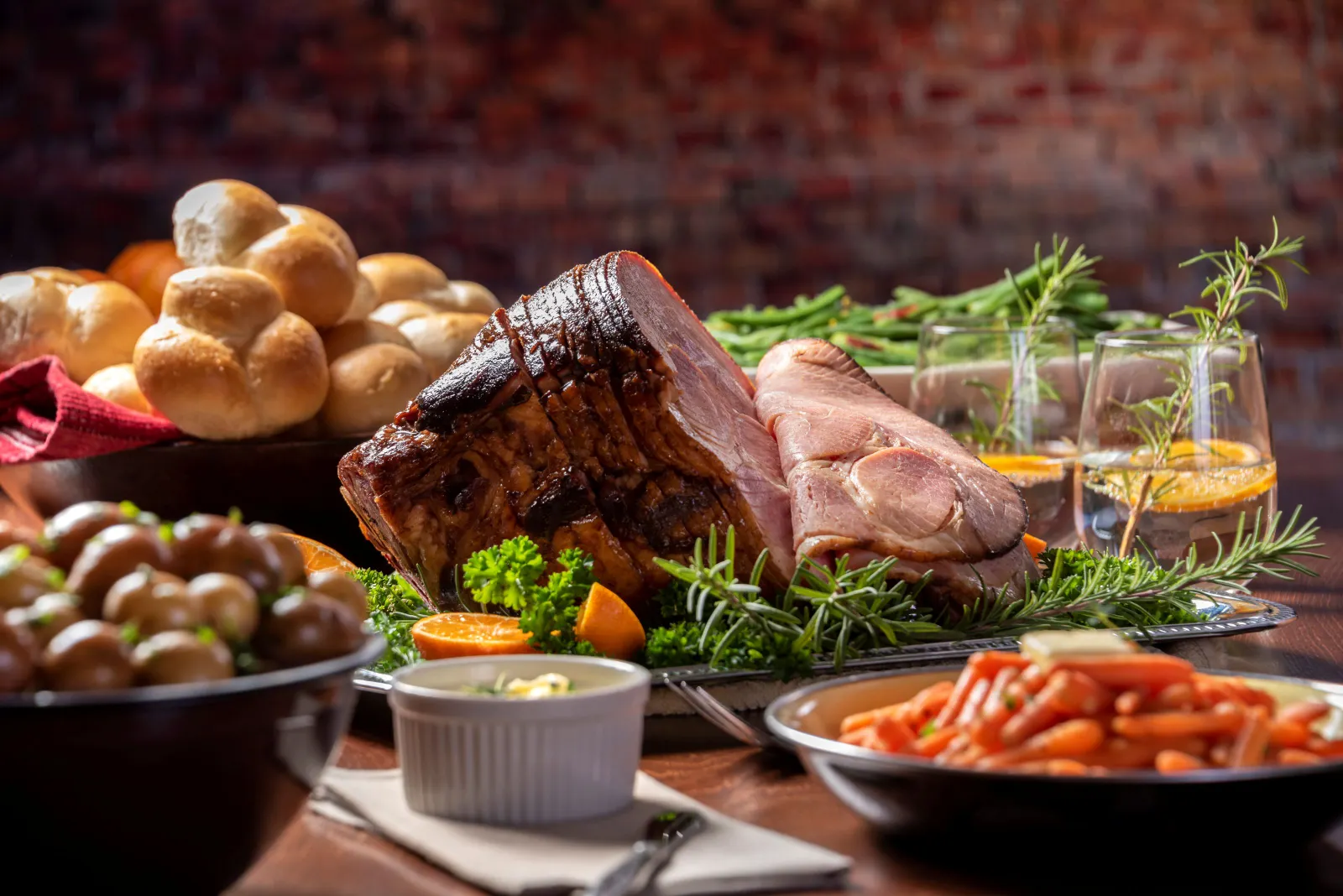 A close up image of an Easter ham and various side dishes like carrots and baby potatoes