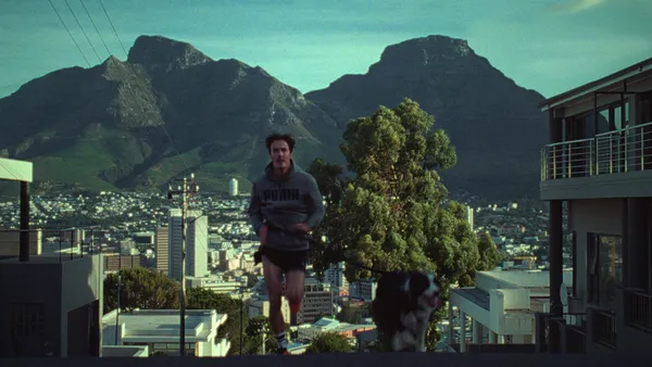 A man in Puma gear runs with a dog with a mountain in the background