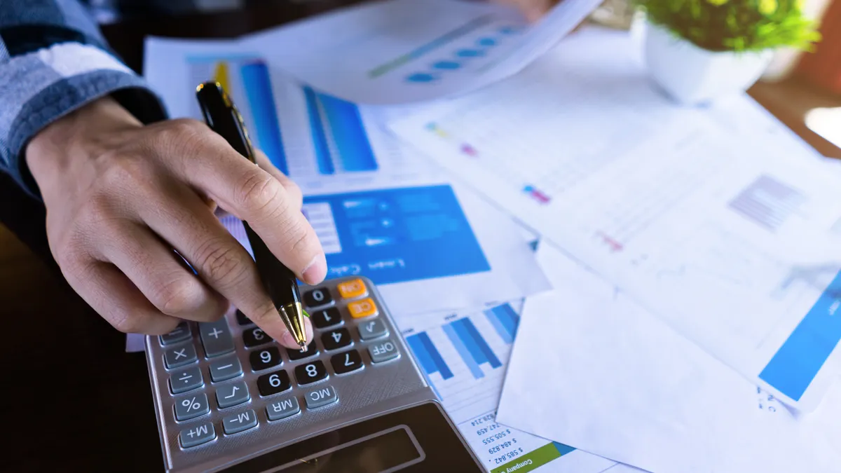 Close up of a person using a calculator and reading paper document about business data.