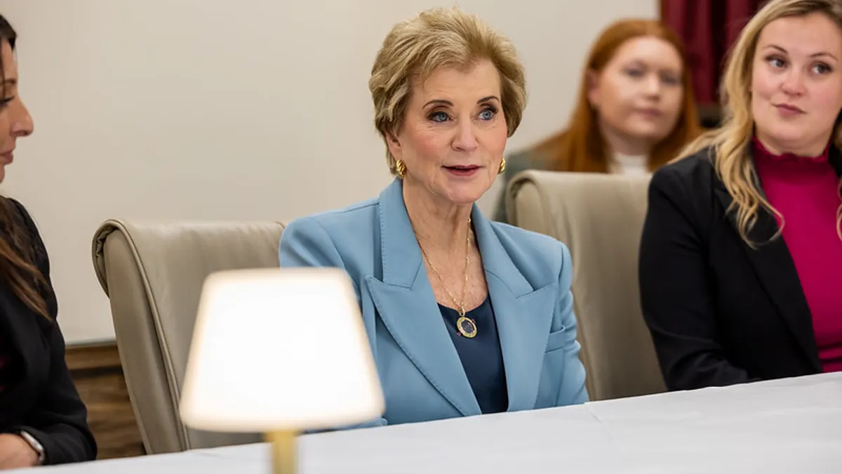 A person is seen sitting at a table with a white cloth. Other people are seated near the person and there is a lamp on the table.