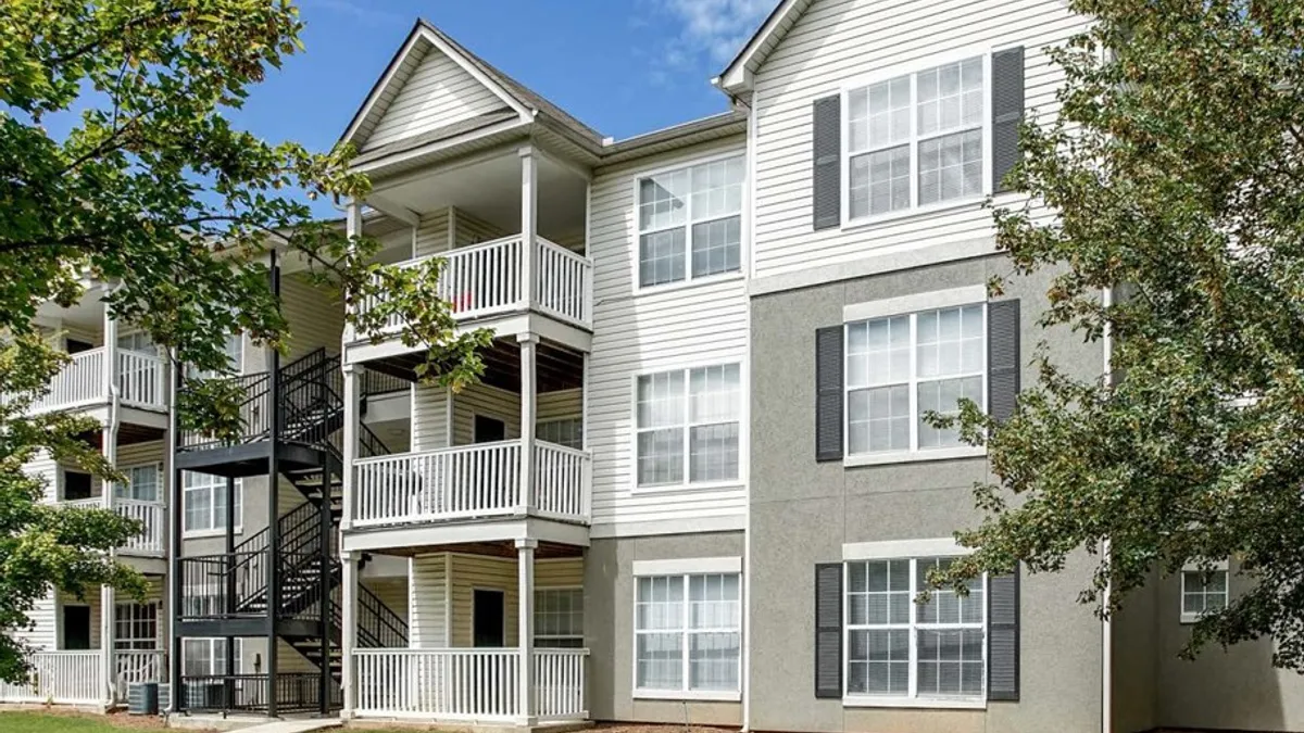 Three-story, light-colored garden-style apartments surrounded by trees and grass