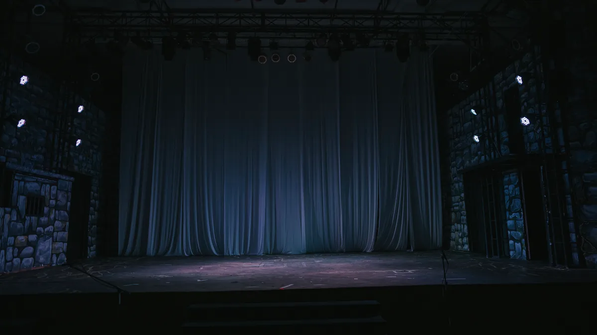 A empty dark theater with a black curtain drawn back.