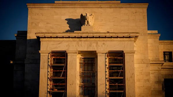 The sun sets on a white stone building that features an eagle sculpture atop a series of columns. Scaffolding is seen between each of the four columns.