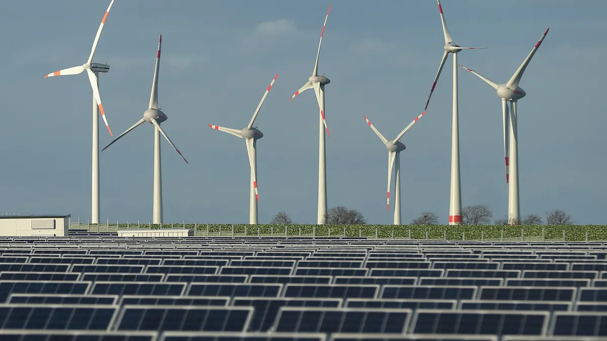 Wind turbines stand behind a solar power park.