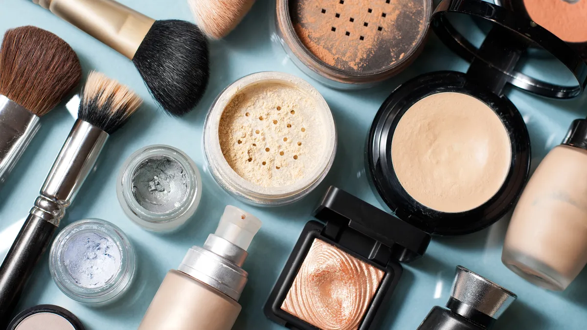 Makeup containers, including powder compacts and makeup brushes, scattered against a blue background