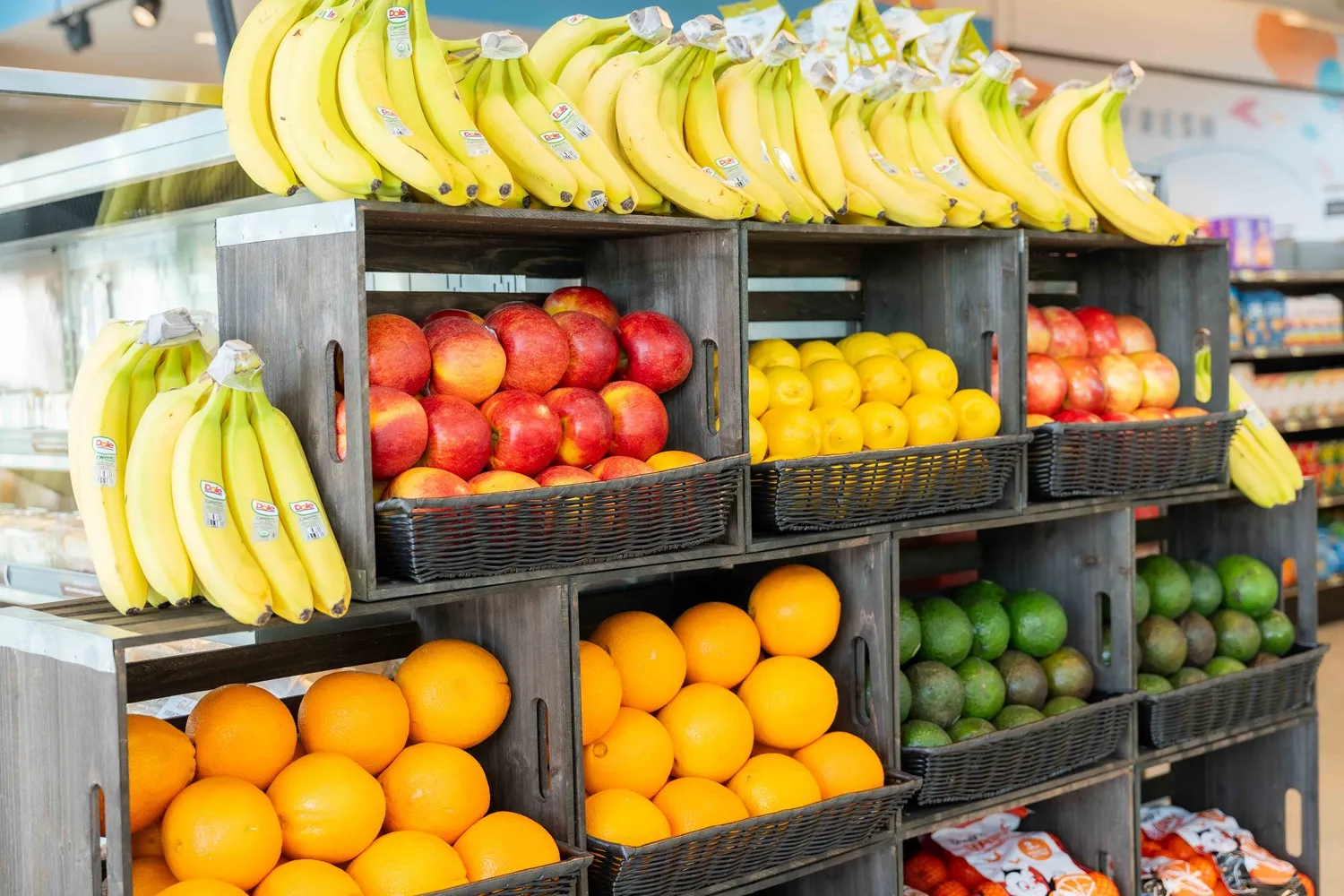 A photo of fruit stacked in boxes inside a store, including bananas, apples, oranges, lemons and limes.