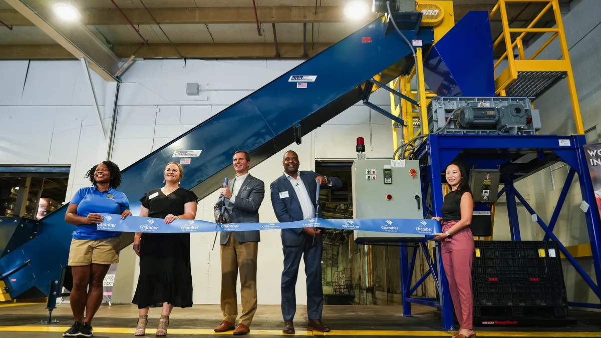 People cut a ribbon in front of a glass crusher machine