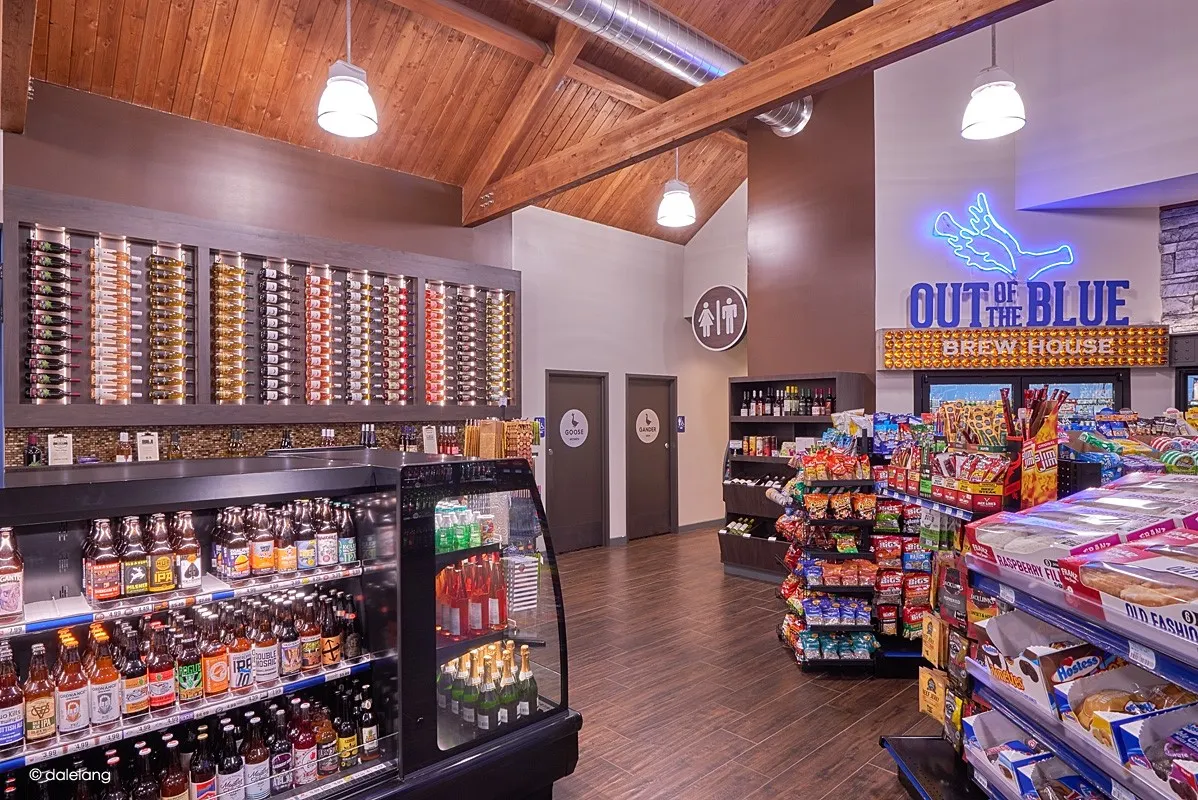 A photo of the interior of a store. There is a beverage cooler to the ledt, restrooms on the far wall in the middle and a beer cave behind some snack shelves to the right. A sign over the door to the beer cave says &quot;out of the Blue brew house.&quot;