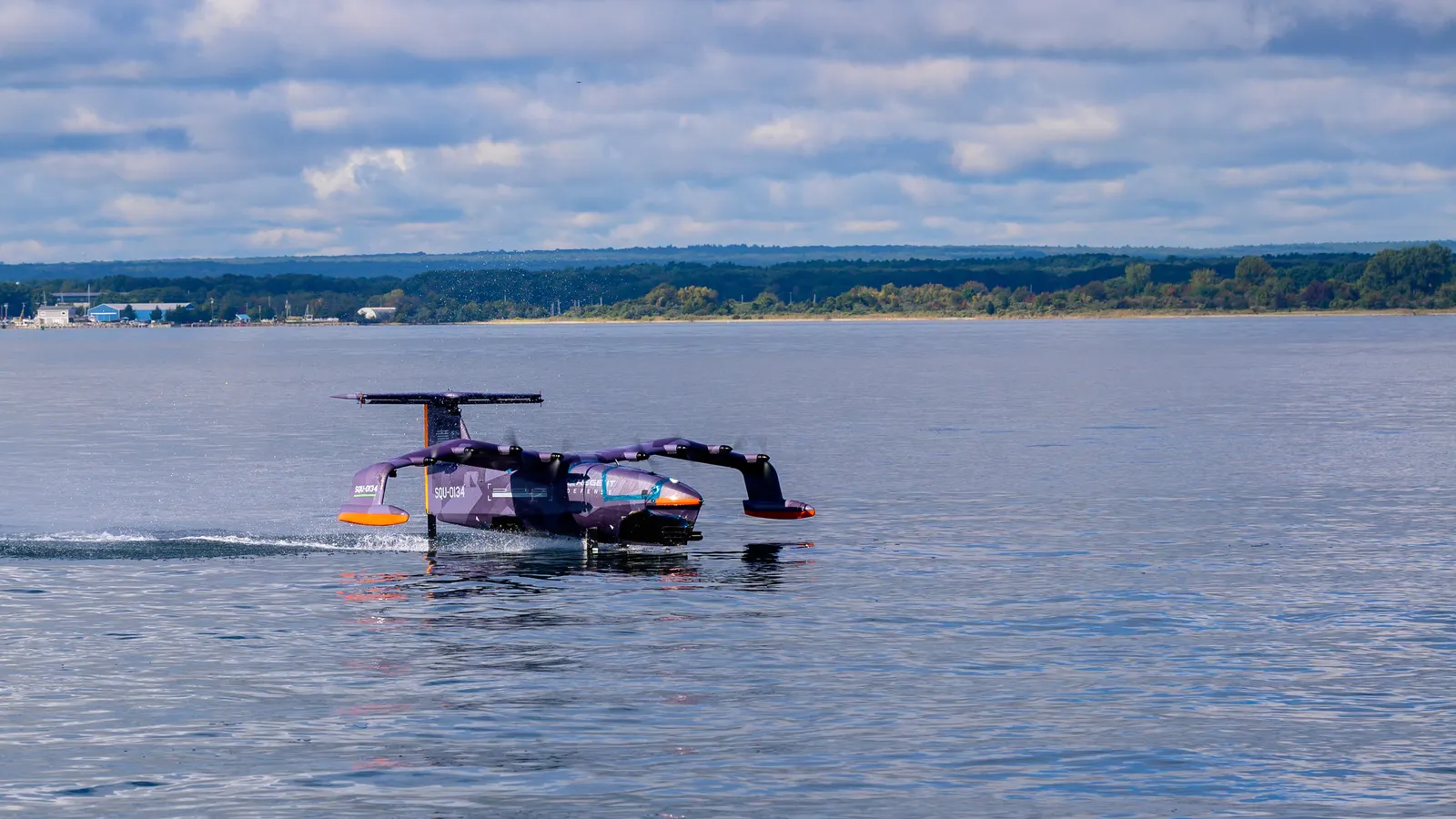 A small purple drone with 2 wings flying just above a body of water.