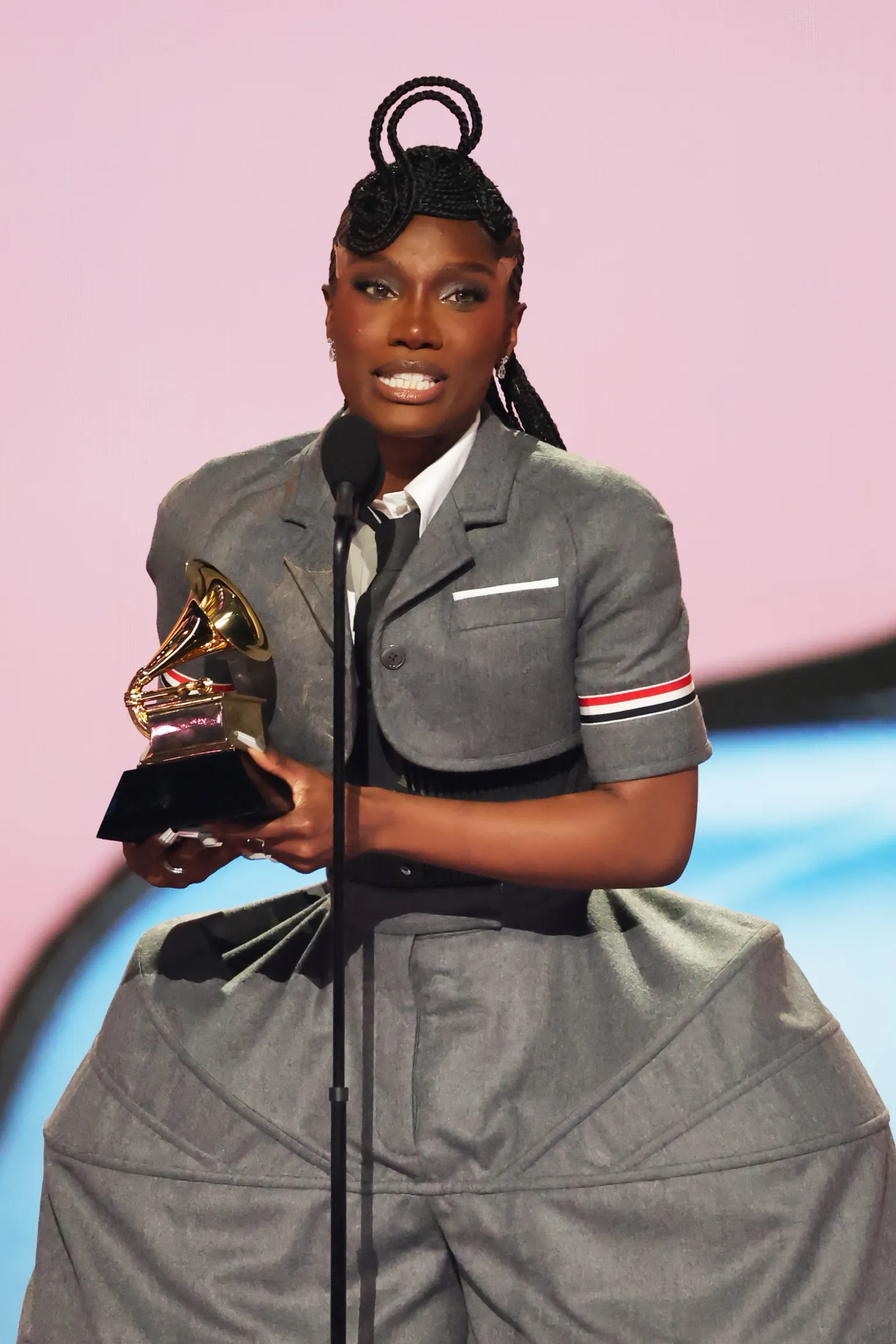 A person wears a wide-hipped suit while holding a Grammy award on a stage.