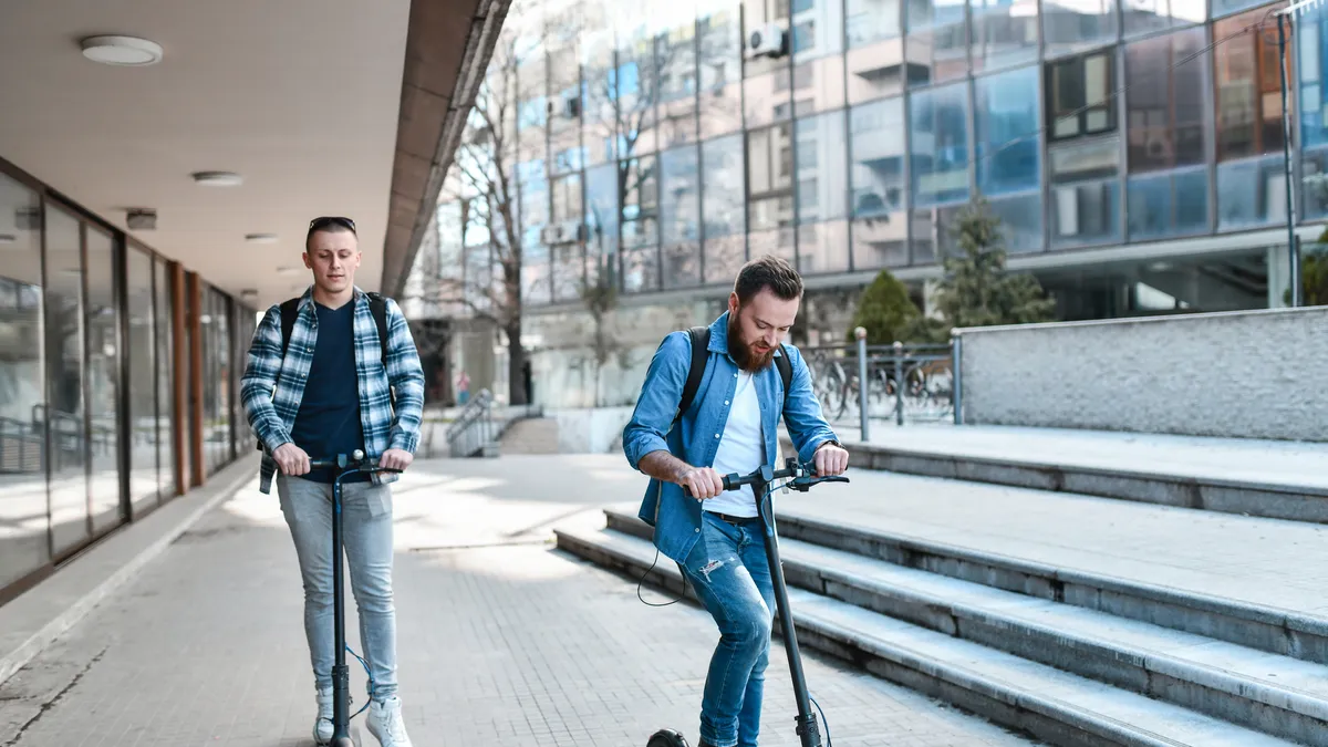 Two young men ride electric scooters on a college campus