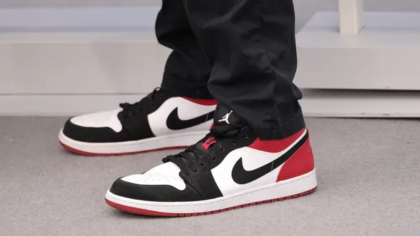 A closeup shot of a person wearing red, white and black sneakers with a Nike logo and black track pants with a Jordan logo.