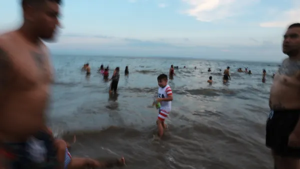 People standing and swimming in the water at a beach.