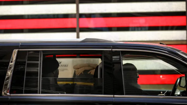 A person driving and a person in the back seat of a black car.
