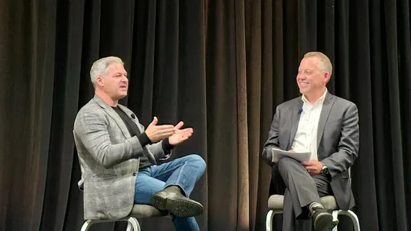 Two people are sitting on chairs on a stage talking