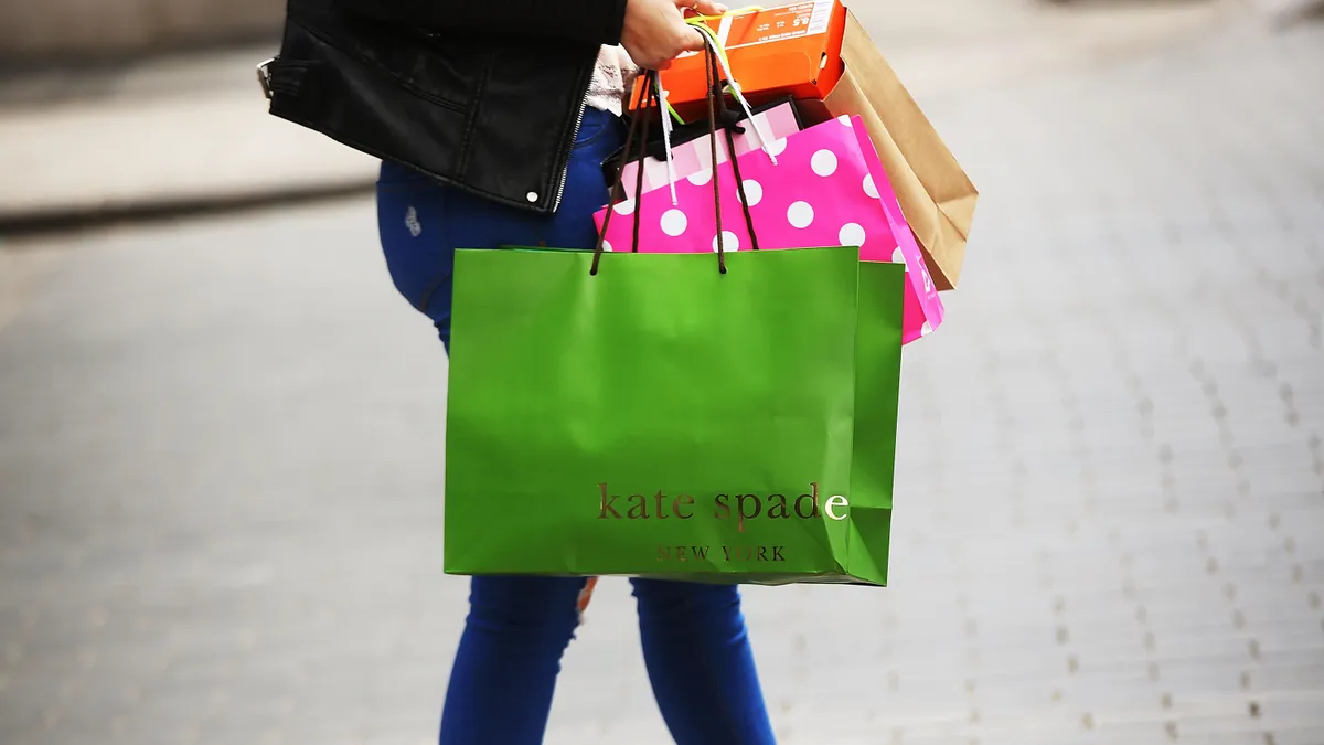 A person is seen holding bags from Kate Spade and other stores.