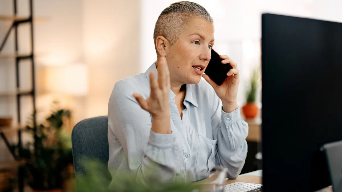 Woman talking over phone while sitting infront of her computer
