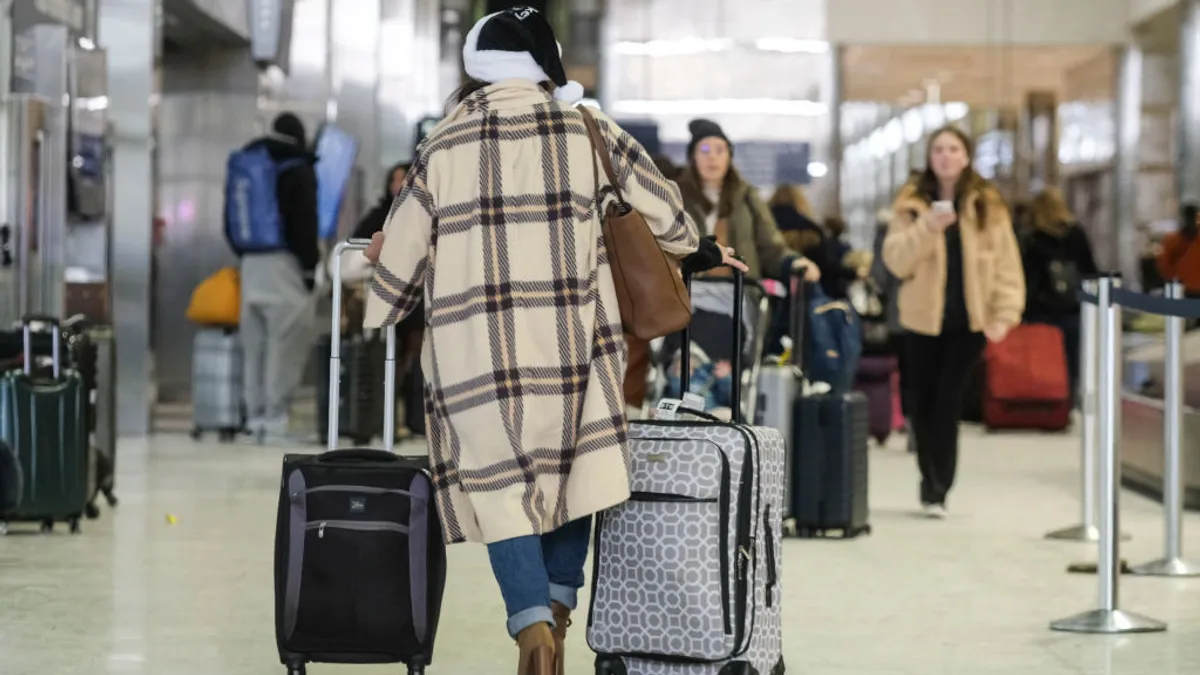 Holiday traveler wearing Santa Claus hat walks through airport terminal with rolling suitcases