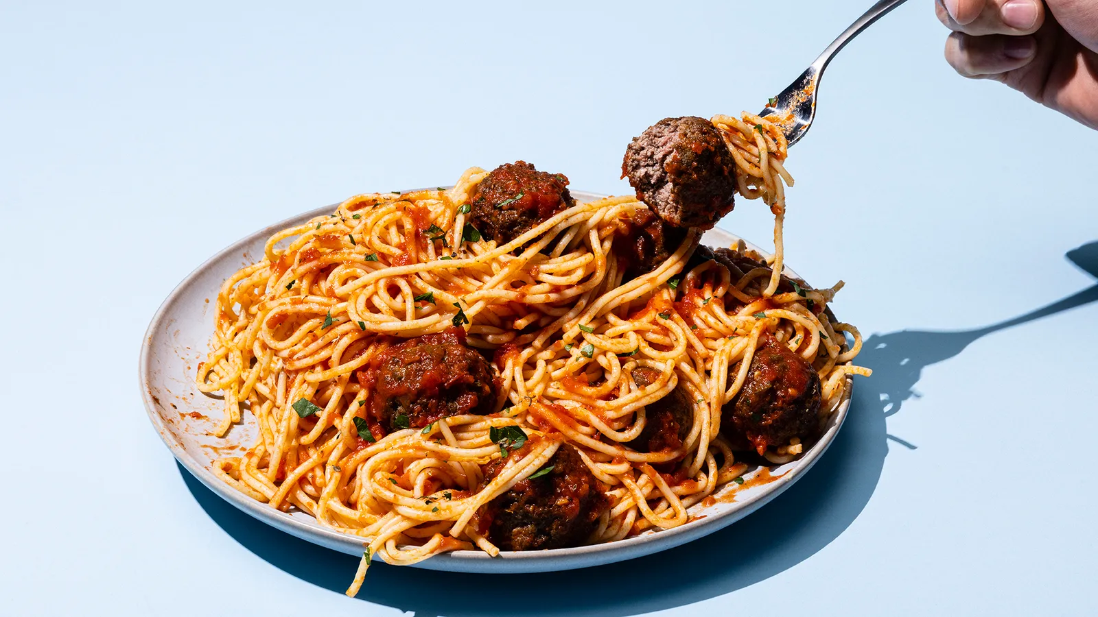 A fork pulls at a spaghetti noodle on a plate of spaghetti and meatballs made from Omeat's cultivated beef.