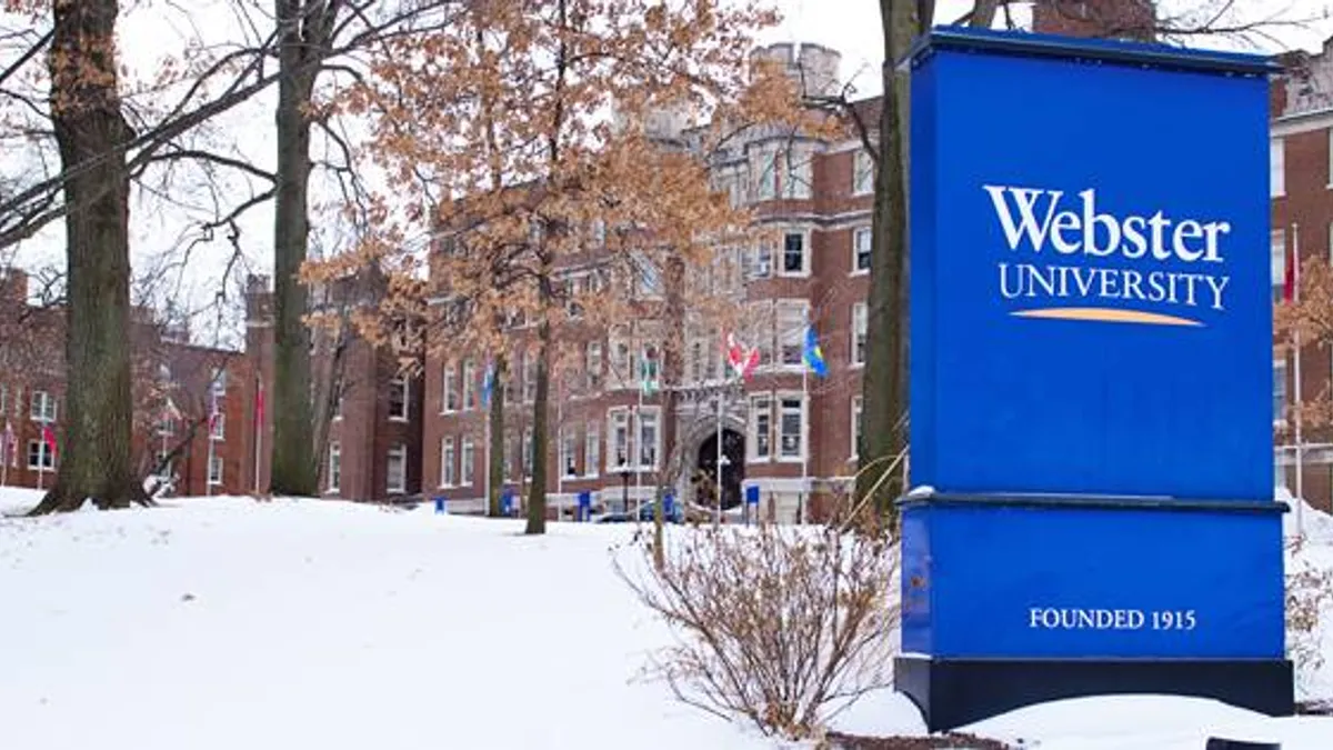 A snow covered landscape, with a sign at the far right of the frame advertising for Webster University.