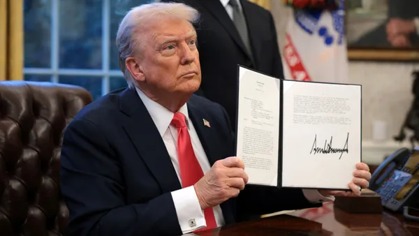 A man holds up a signed paper while sitting behind a desk.