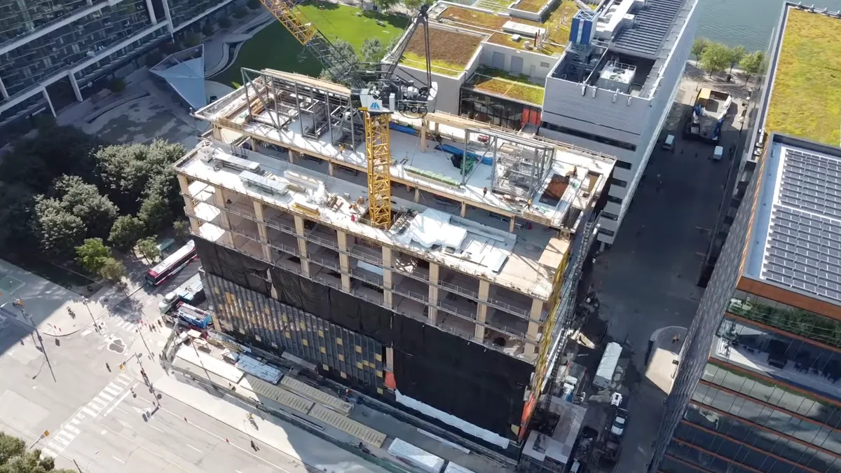 An aerial shot of an under-construction building that's under construction. A crane and several open areas of the building are being built throughout the image.