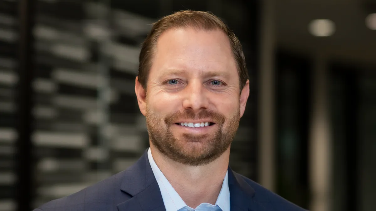 a photo of iRhythm CEO Quentin Blackford smiling. He is bearded and wearing an open-collared shirt and suit jacket.