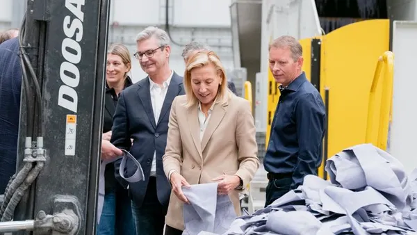 A group of people in a Gen Phoenix factory stand by a pile of material. A person holds the material.