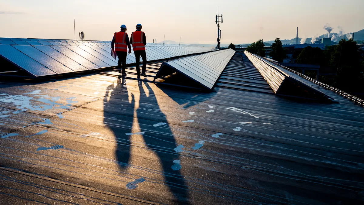 Rear view of engineers walking along the rows of photovoltaic panels on a rooftop of a solar plant.