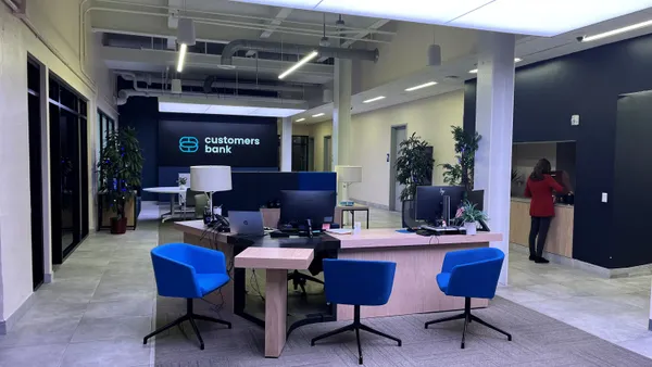 The interior of a modern office space is shown, with tables and chairs and "Customers Bank" on a back wall.