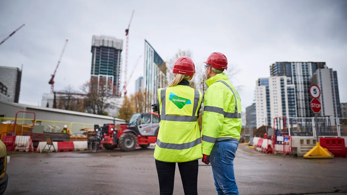 Two construction workers in safety gear look at cranes.