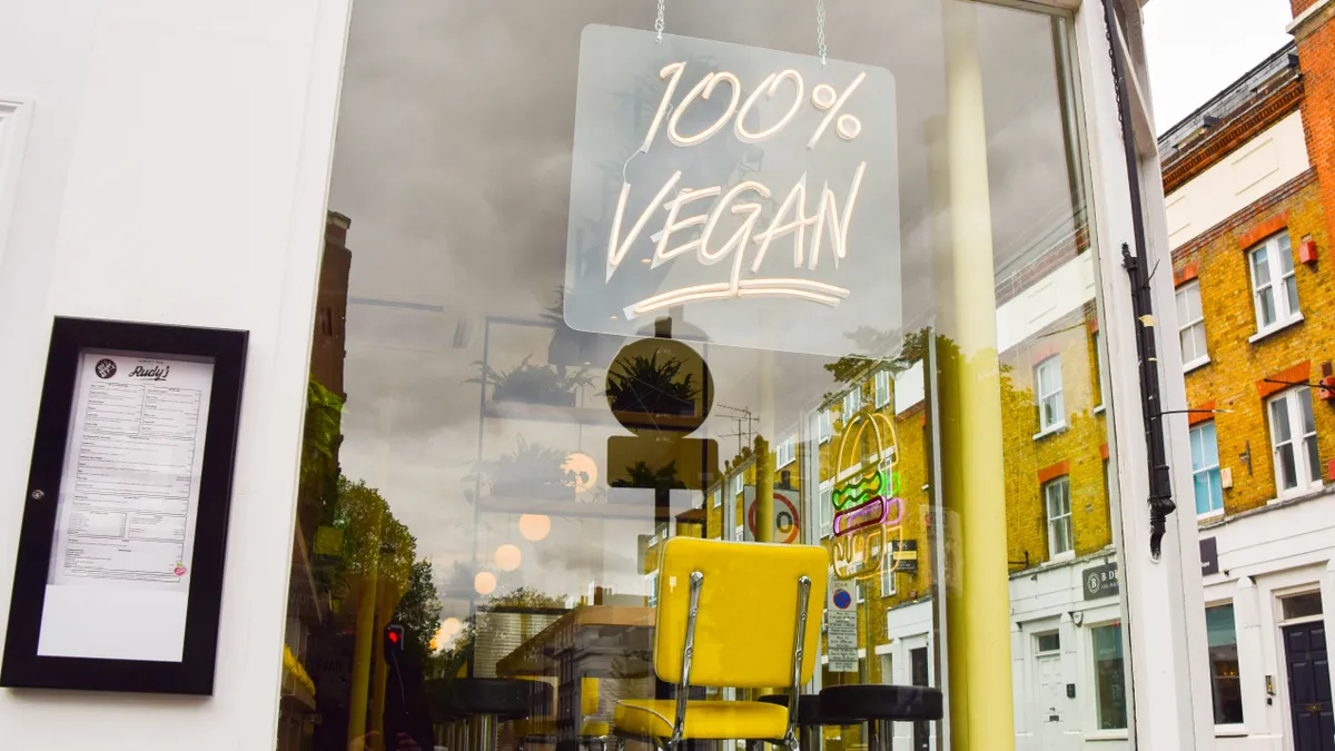 Outside picture of the inside of a store, a sign that says 100% vegan with yellow and black chairs