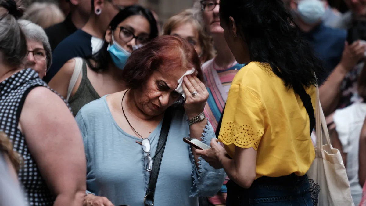 A woman wipes her brow in a crowd of people.