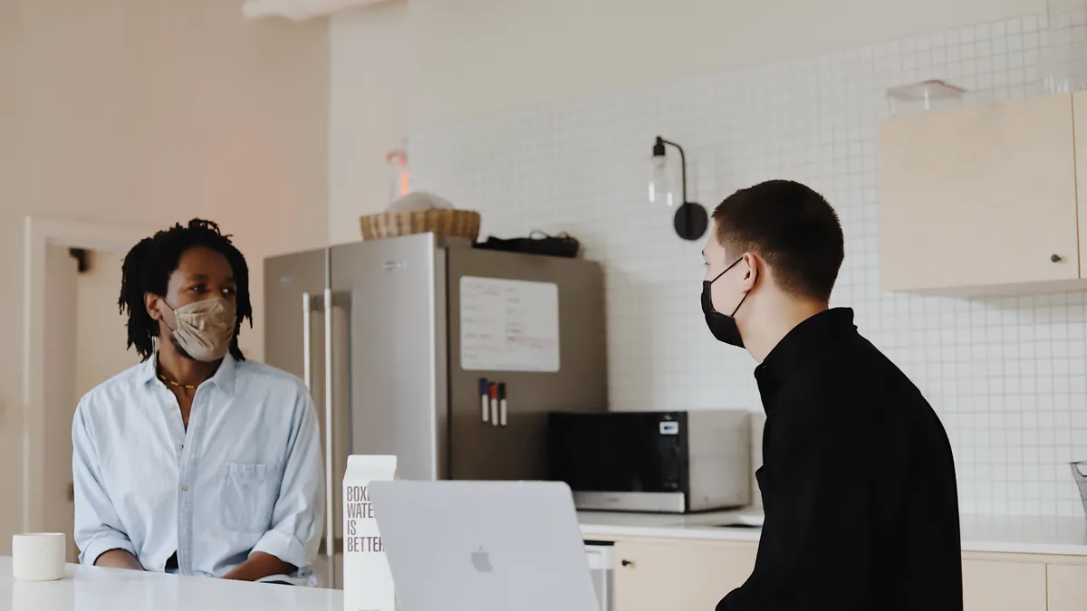 Two employees wearing masks talk together in an office