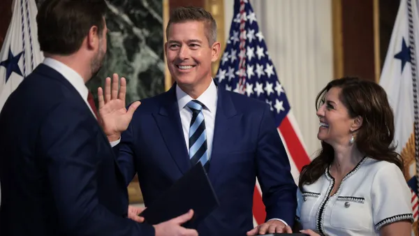 Three people stand by U.S. flags as one raises his hand, the other on a bible.