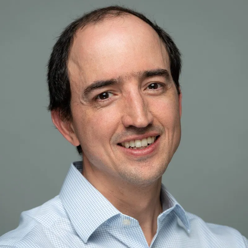 A smiling white man in a white shirt with a receding hairline.