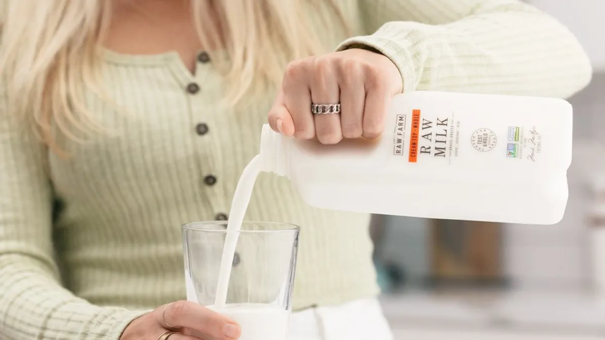 A close up of a woman pouring raw milk into a glass