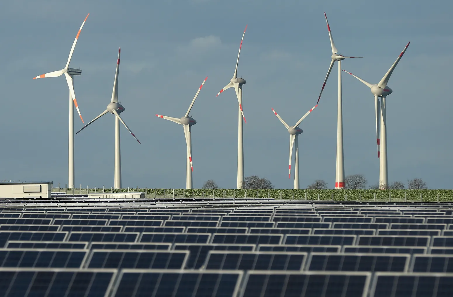 Wind turbines stand behind a solar power park.