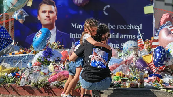 A mother and child crouch in front of a makeshift Charlie Kirk memorial