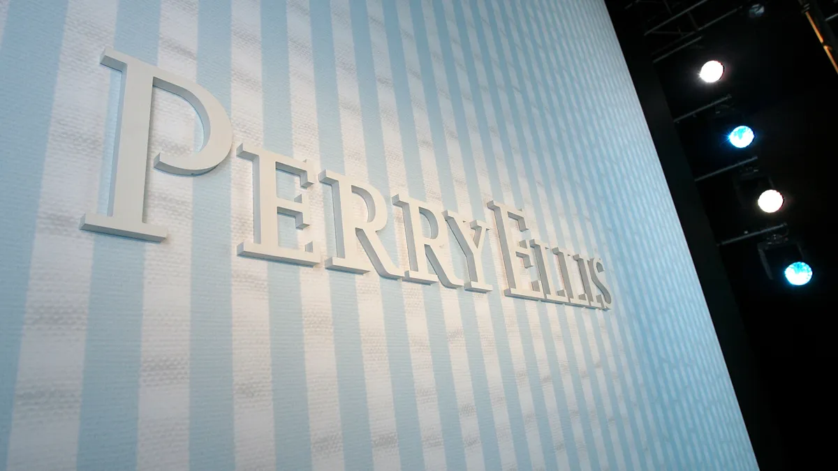 The Perry Ellis logo is seen against a blue and white striped wall.