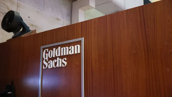The Goldman Sachs name and logo is shown on a wooden half wall.