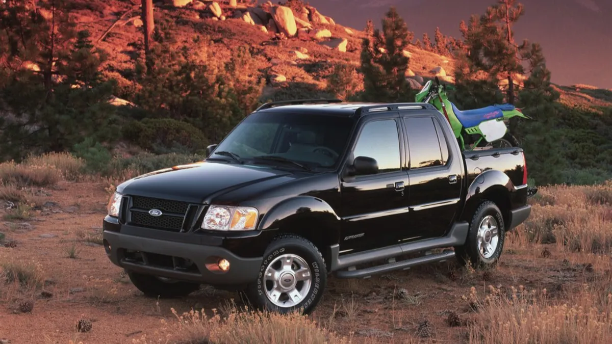A black 2001 Ford Explorer Sport Trac loaded with activity gear sits on grass, with a mountain backdrop.