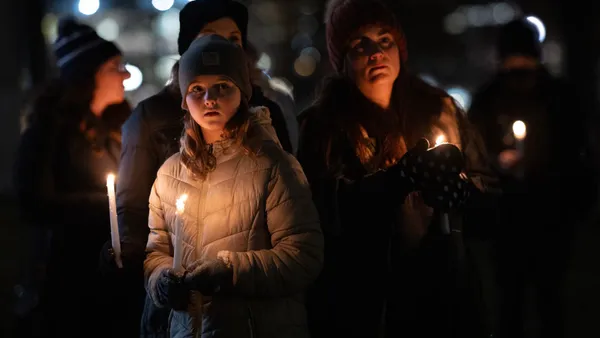 People are standing outside in the dark, holding candles and wearing coats and hats