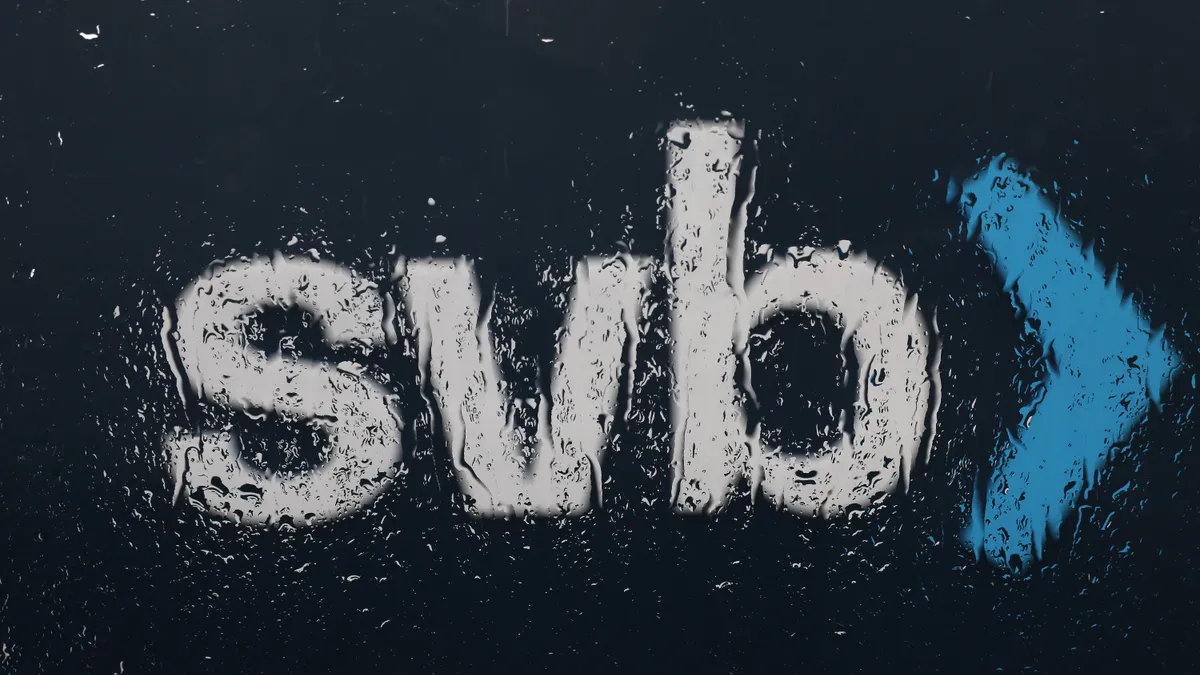 A sign showing a company logo seen through a rain-covered window.