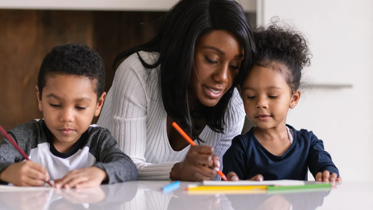 A parent helps two children on their homework.